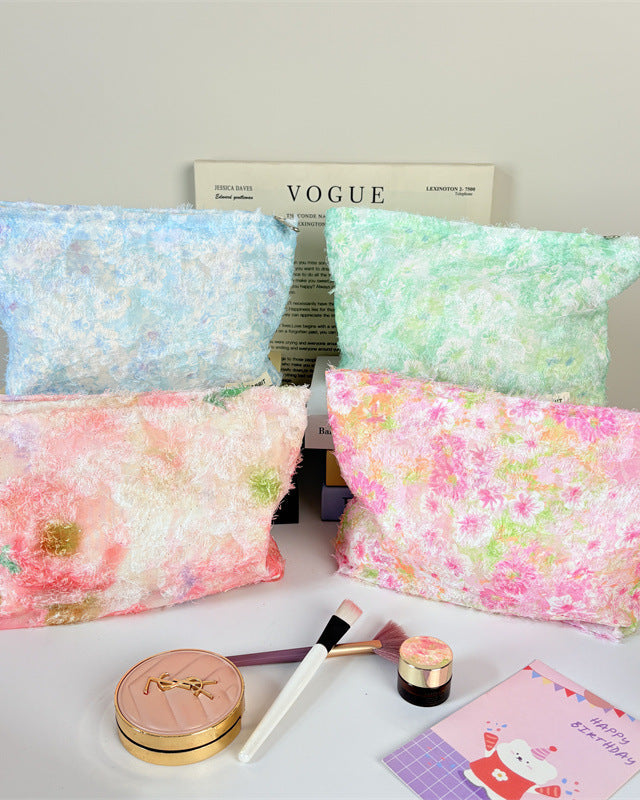 Four floral-patterned pouches on a table with makeup items and a Vogue magazine.