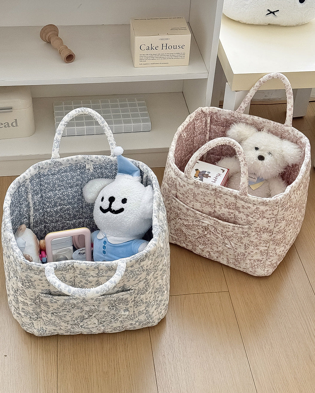 Two fabric baskets with toys on a wooden floor, one in front of a white shelf.
