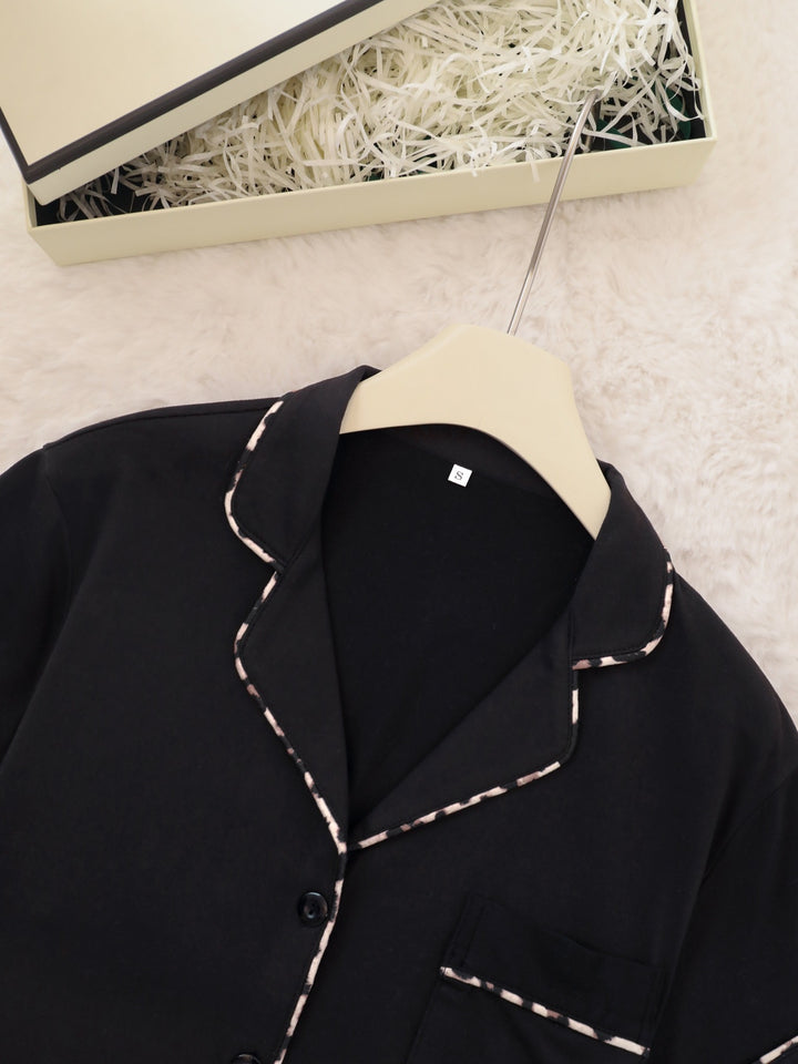 Black shirt with white stitching on a hanger against a neutral background