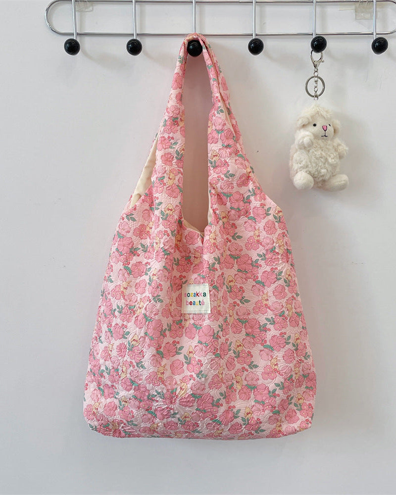 Floral-patterned bag hanging on a hook with a small plush toy beside it.