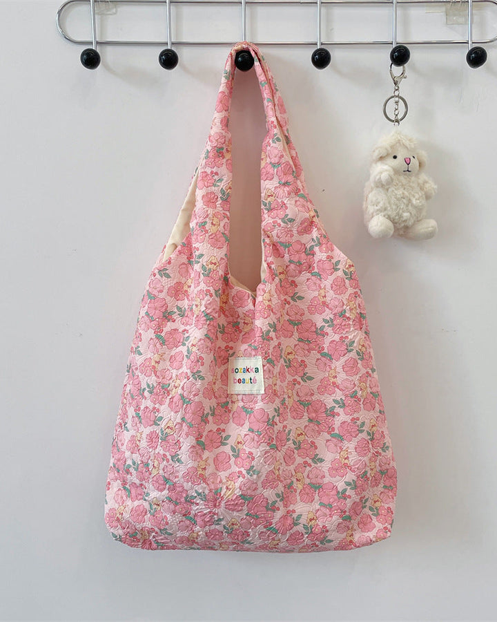 Floral-patterned bag hanging on a hook with a small plush toy beside it.