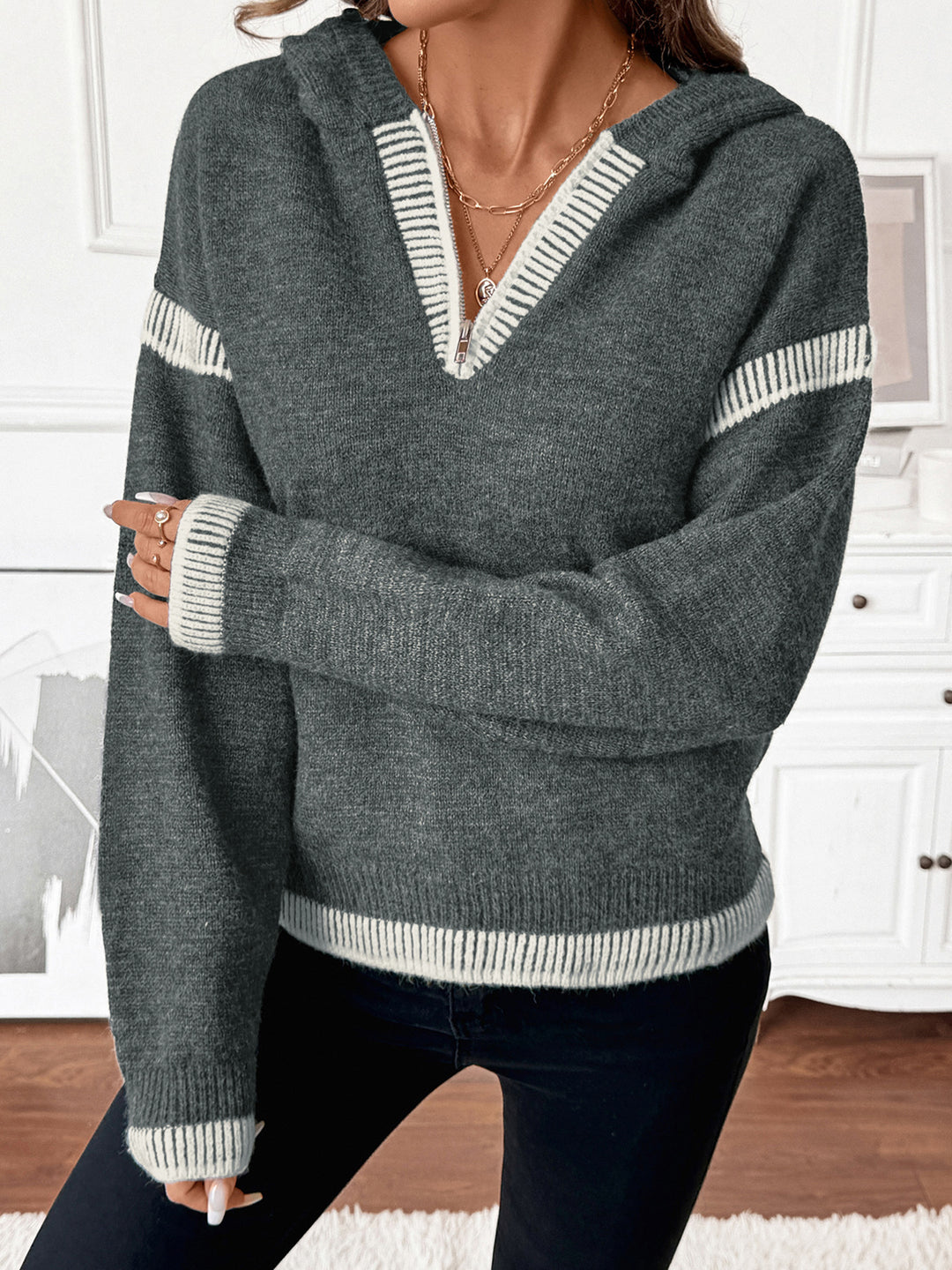 Person wearing a gray sweater with white stripes in a room with white walls and wooden floor.