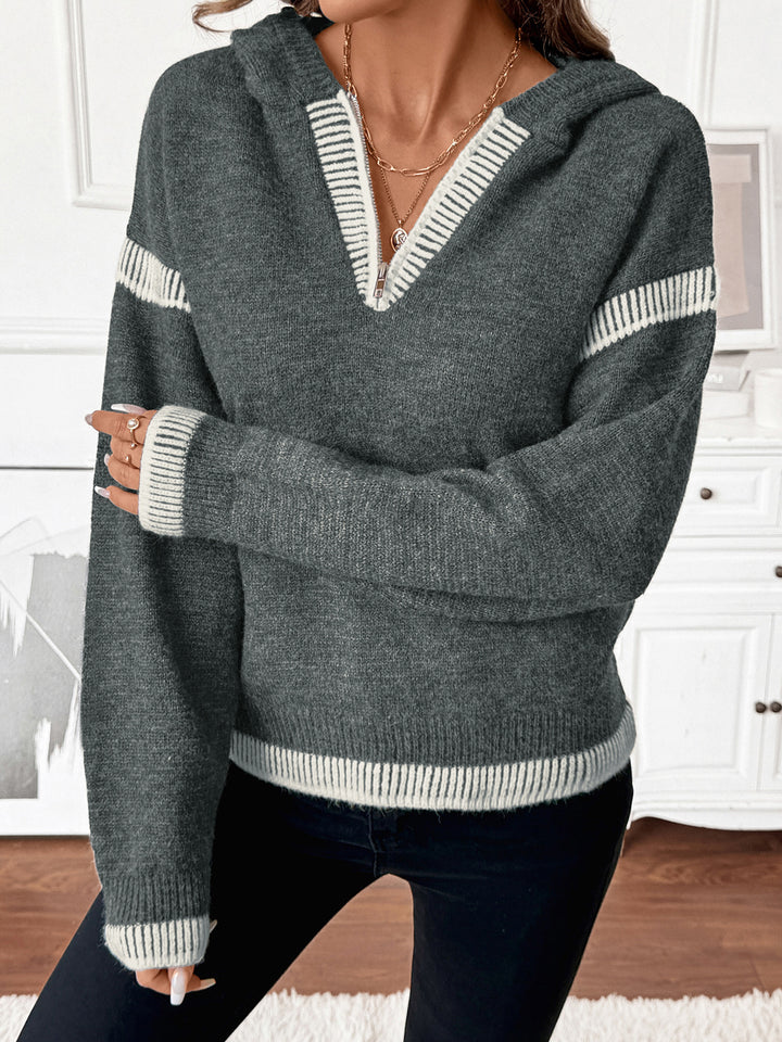 Person wearing a gray sweater with white stripes in a room with white walls and wooden floor.