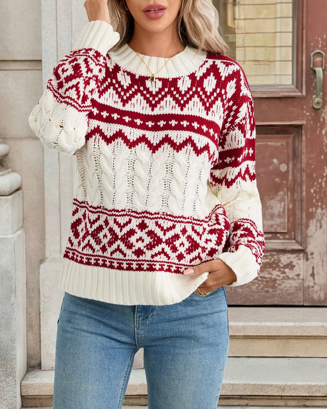 Woman wearing a white sweater with red pattern standing in front of a wooden door.