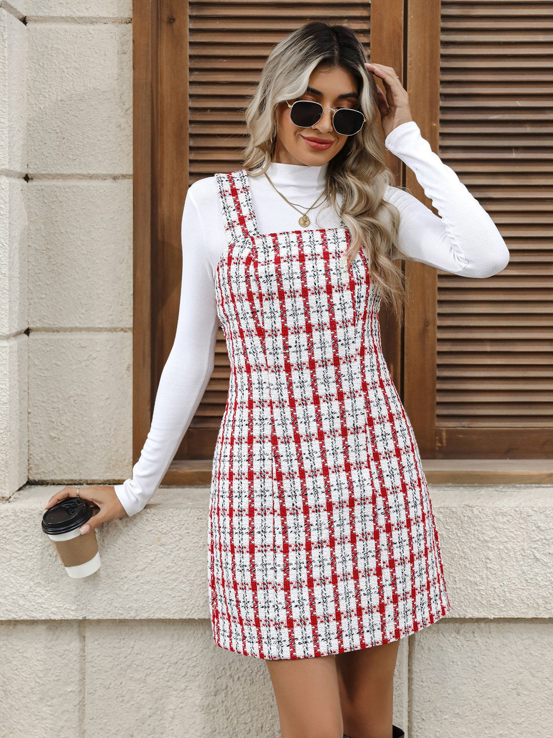 Woman wearing a red and white checkered dress holding a coffee cup against a stone wall.