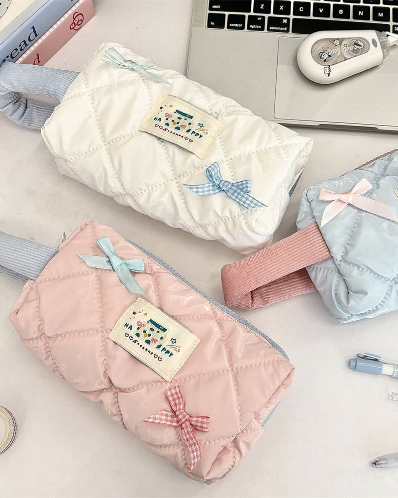 Three quilted pouches in white, pink, and blue with decorative bows on a desk.