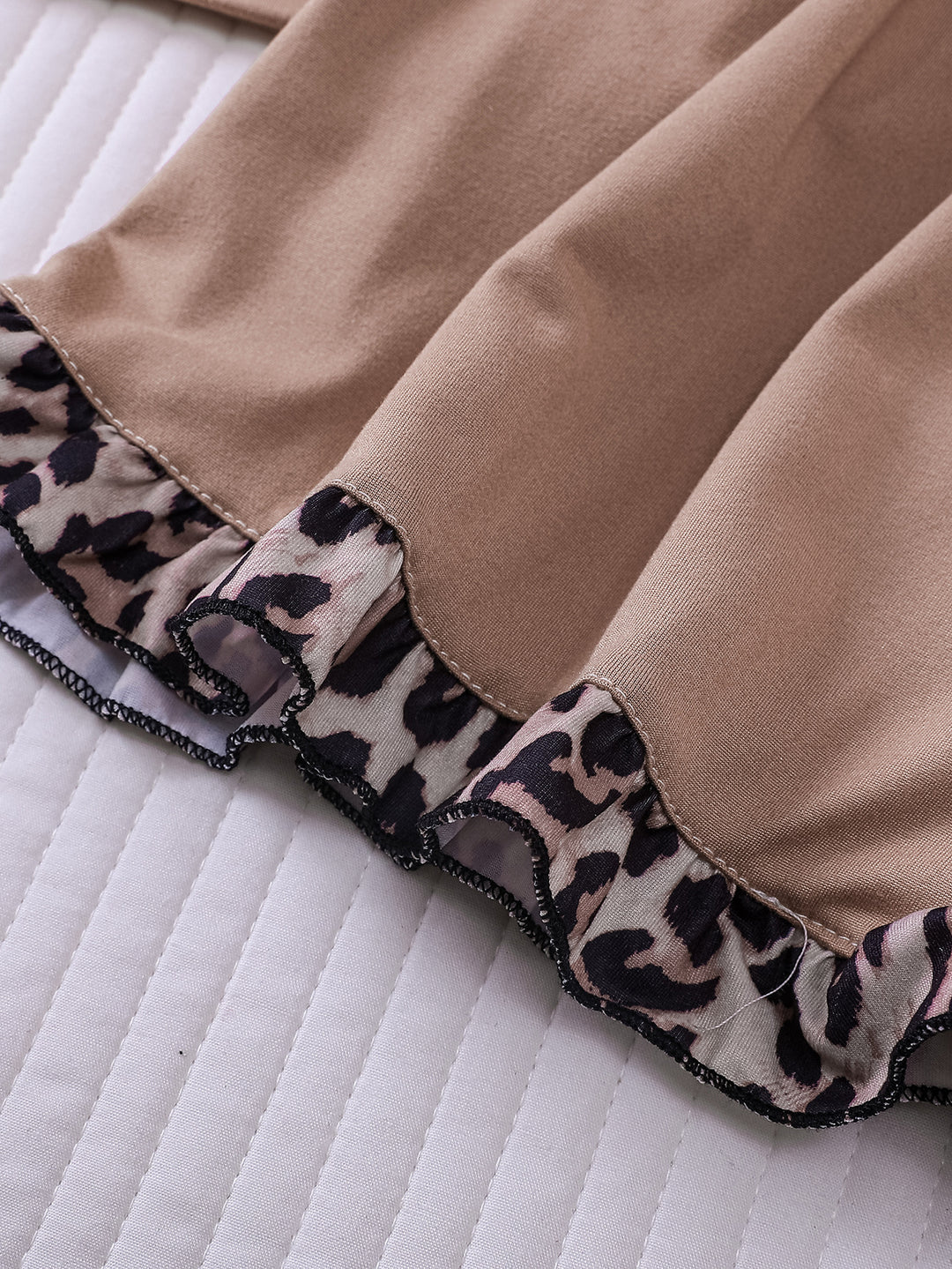 Close-up of a brown fabric with leopard print trim on a white quilted surface