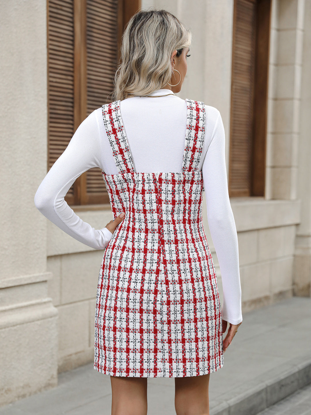 Woman wearing a red and white checkered dress with a white long-sleeve shirt outdoors.