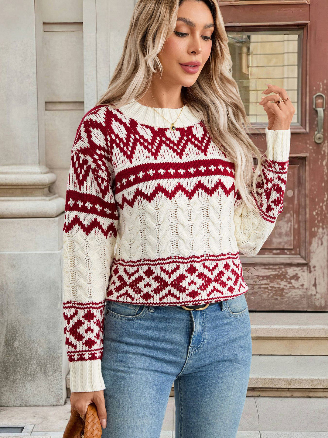 Woman wearing a red and white patterned sweater with blue jeans standing outdoors.