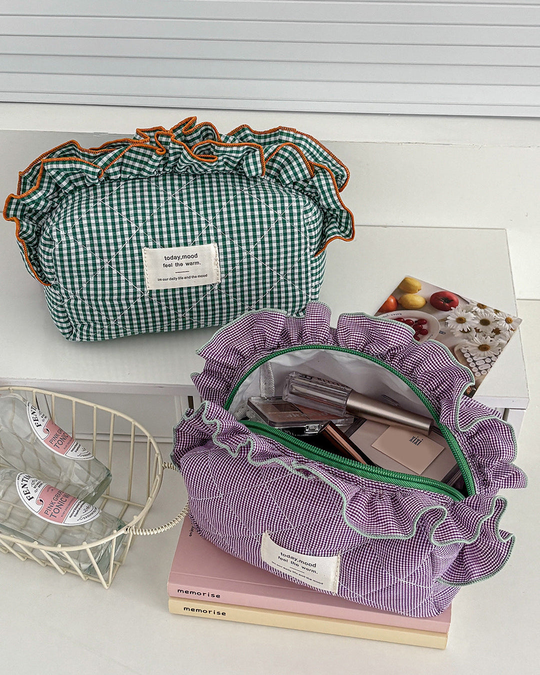 Two cosmetic bags, one green checkered and one purple with ruffles, on a white surface.