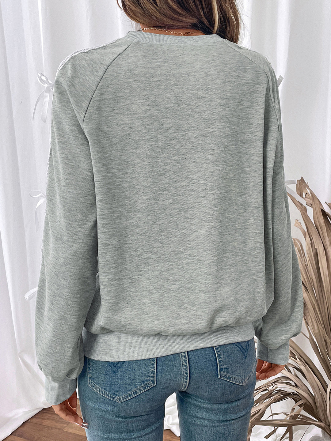 Person wearing a gray sweatshirt and blue jeans standing against a white curtain.