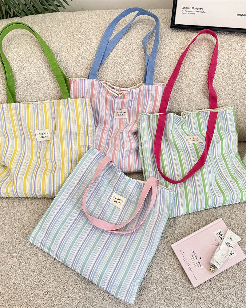 Four colorful striped tote bags on a beige surface with a framed picture in the background.