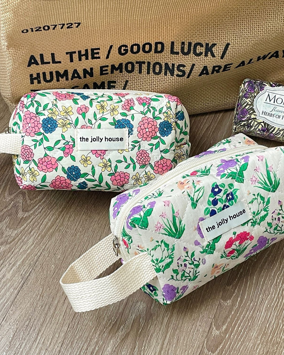 Two floral-patterned bags with 'the jolly house' branding on a wooden surface, with a Monpari soap in the background.