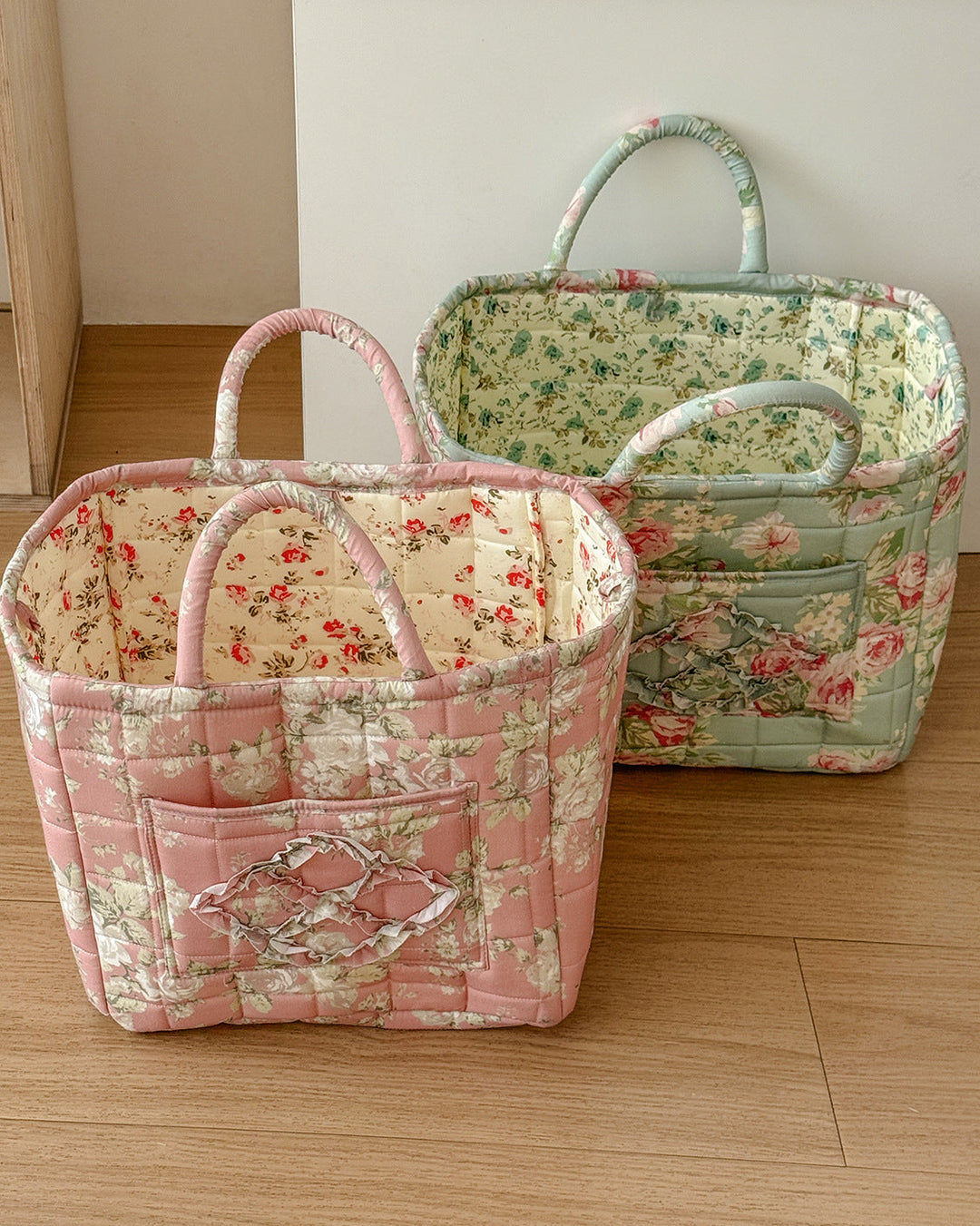 Two floral-patterned fabric baskets on a wooden floor.