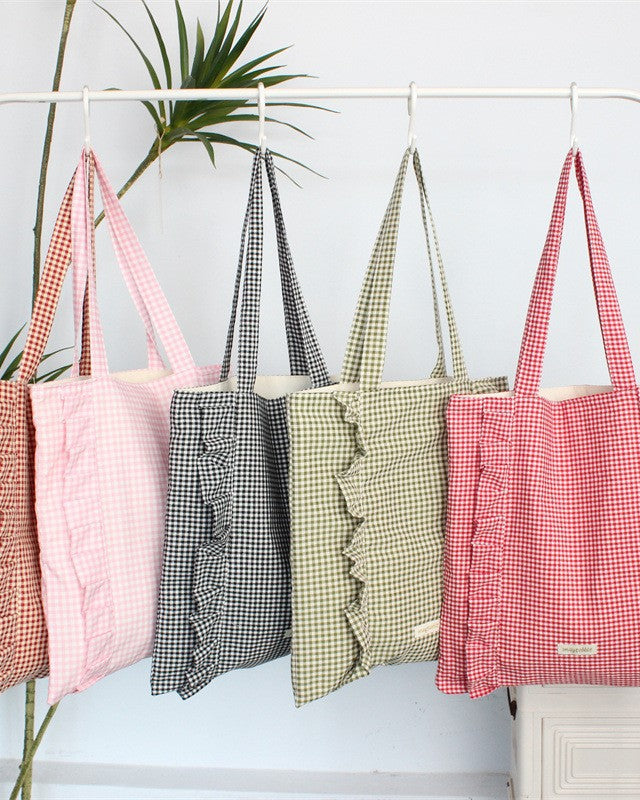 Set of gingham patterned bags hanging on a rack with a plant in the background.