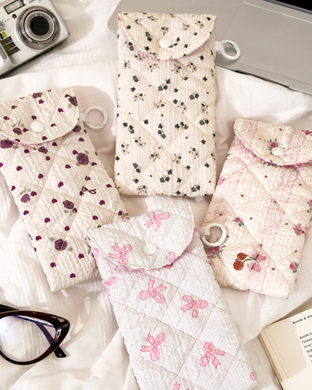 Floral-patterned pouches on a white surface with a camera and glasses.