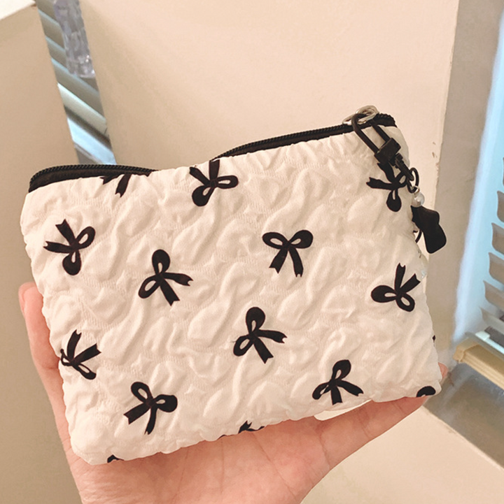 White pouch with black bow patterns held in a hand against a neutral background