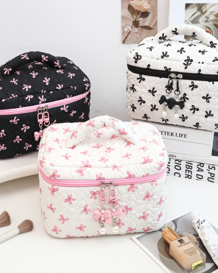 Three cosmetic bags with bow patterns on a surface with magazines and makeup items.