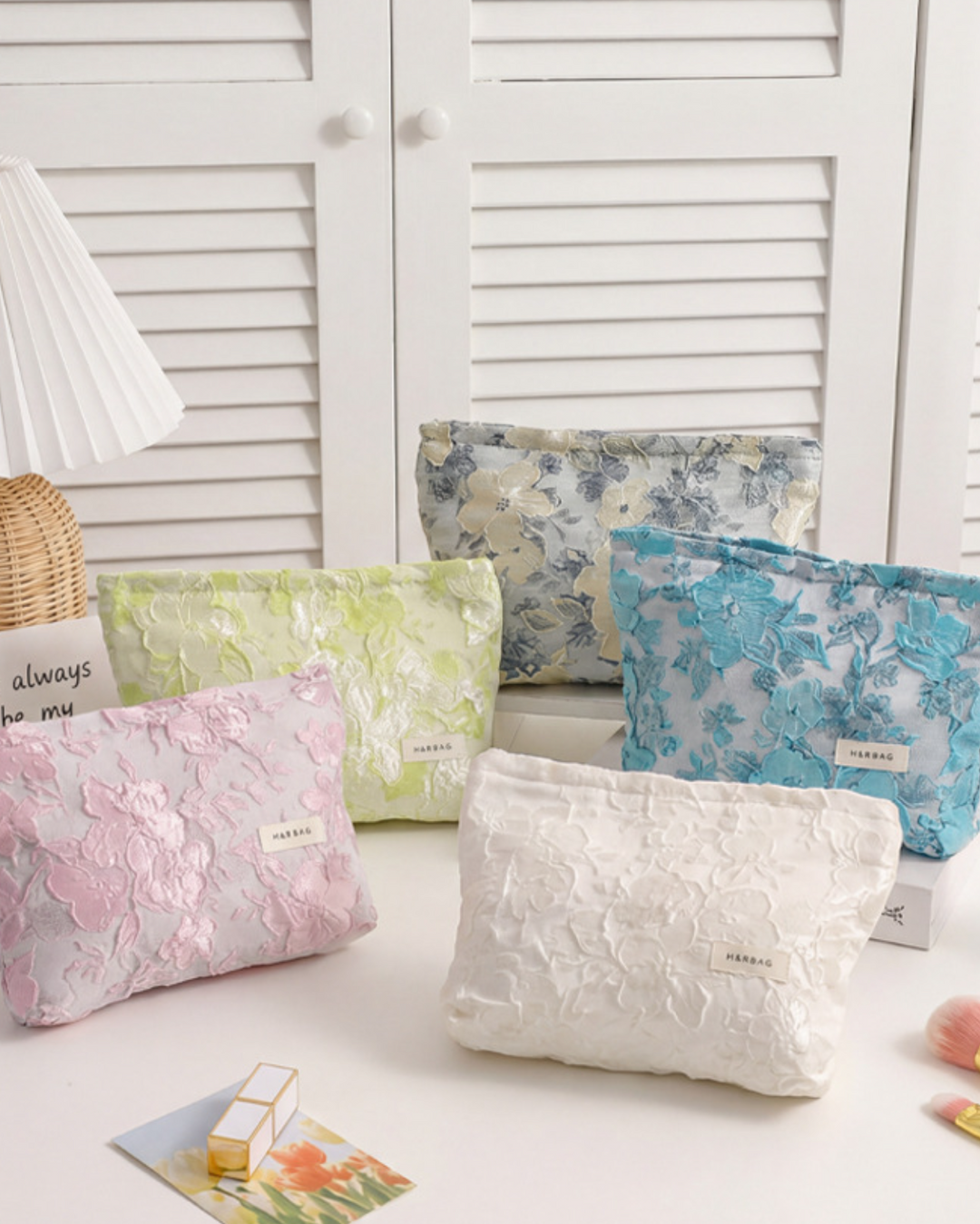 Set of floral-patterned pouches on a light surface with a lamp and shutters in the background.