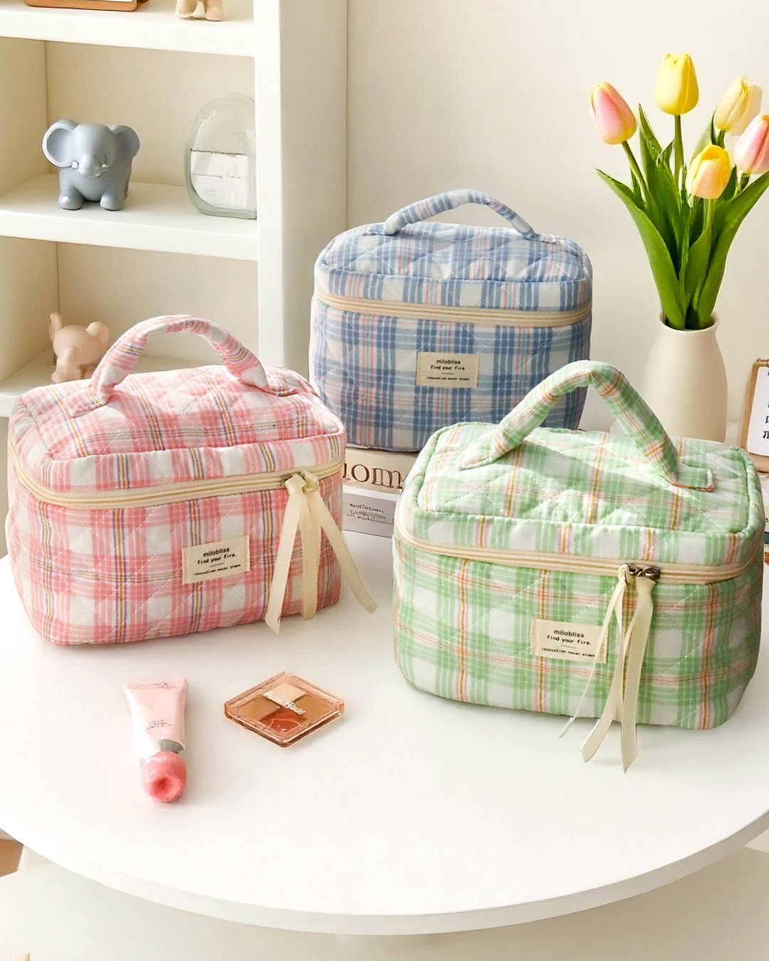 Three checkered bags in pink, blue, and green on a white surface with a vase of tulips in the background.
