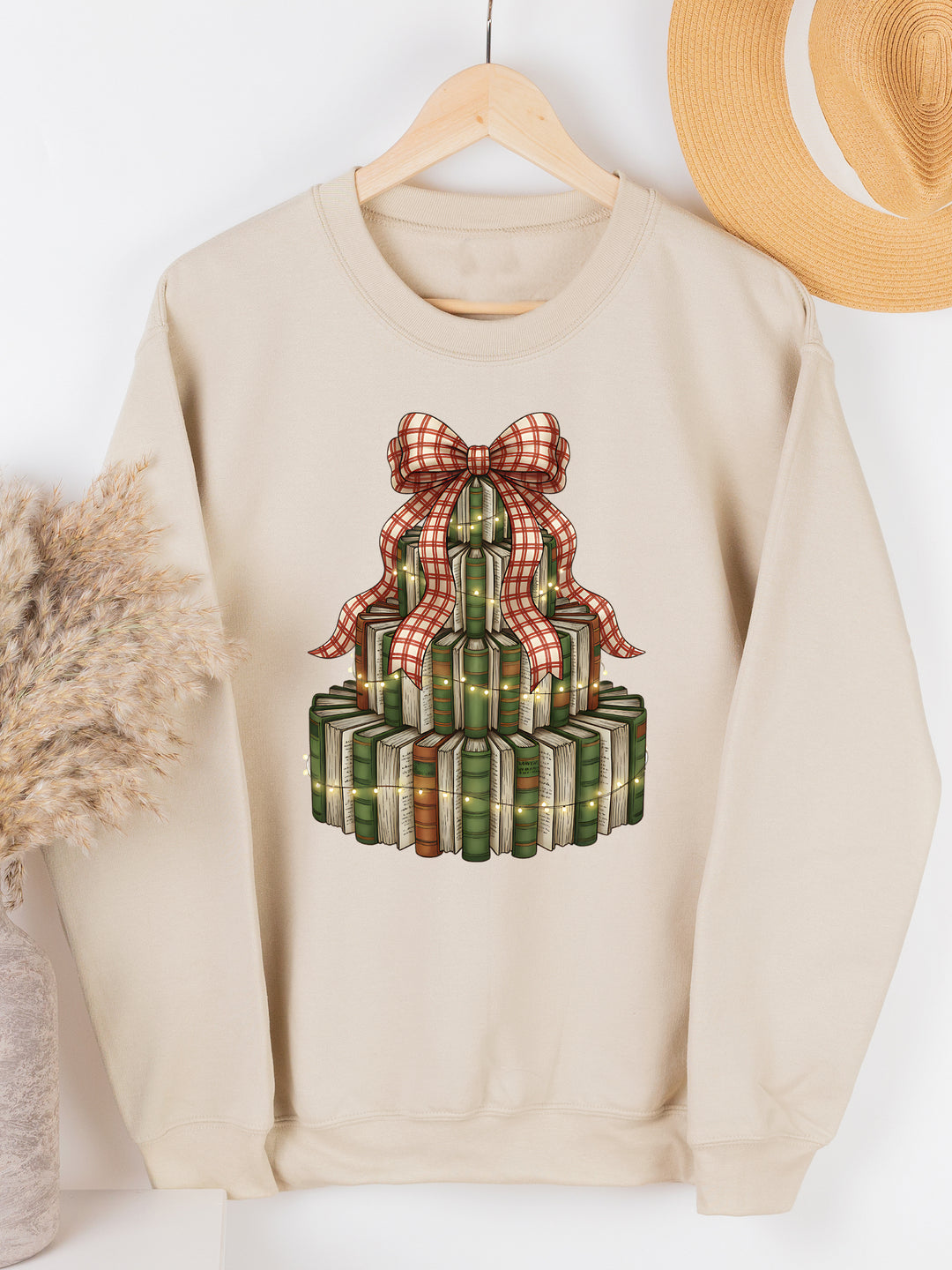 Beige sweatshirt with a Christmas-themed design of gift boxes and a bow, hanging on a wooden hanger against a white background.