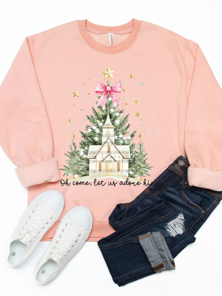Pink sweatshirt with Christmas tree and church design, paired with jeans and sneakers on a white background.
