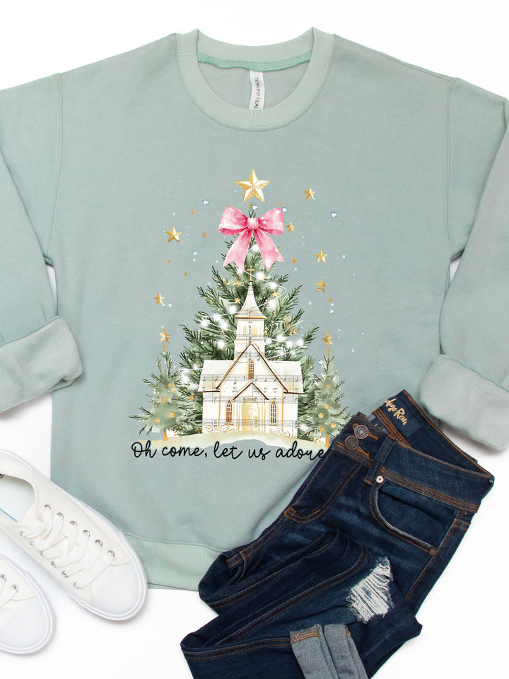 Light blue sweatshirt with Christmas tree and church design, paired with jeans and white sneakers on a white background.